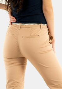 Chinos beige avec une texture lisse, dotés d'une ceinture tressée blanche, de poches arrière et d'une coupe ajustée, vus de dos.