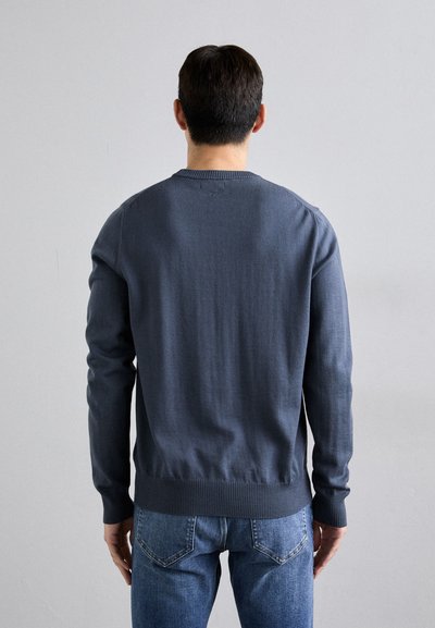 Pull en maille bleu marine avec un col rond, des poignets et un ourlet côtelés, associé à un jean en denim bleu. Design simple et texturé.