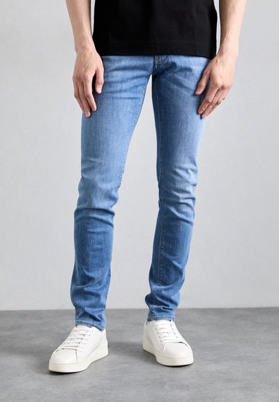 Hellblaue Skinny Jeans mit einem ausgewaschenen Look, aus Denim gefertigt, kombiniert mit weißen Sneakers in niedriger Ausführung, die eine glatte Textur und ein minimalistisches Design aufweisen.