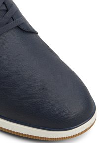 Navy blue synthetic shoe with a textured upper, round toe, and white sole featuring a subtle ridged pattern. Laces are dark matching color.