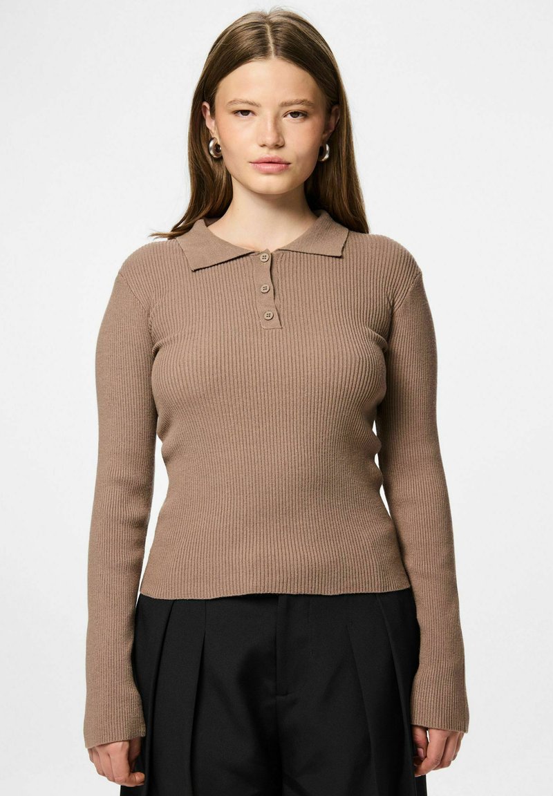 Top marrón de manga larga y acanalado con cuello y tres botones en la parte frontal. Presenta un ajuste ceñido y una tela texturizada. Combinado con pantalones negros.