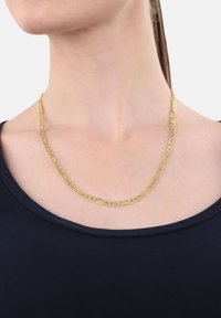 Collana di catena d'oro con anelli grandi e piccoli alternati indossata attorno al collo di una donna su un top blu navy, sfondo bianco.