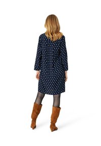 Marineblaues Kleid mit cremefarbenen Pünktchen, langen Ärmeln und entspannter Passform. Getragen mit braunen Wildleder-Stiefeln bis zum Knie. Strukturiert, knöchellanges Design.