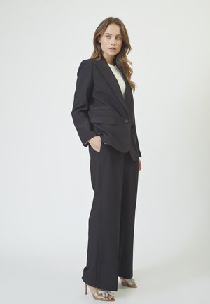 Black tailored suit featuring a single-button blazer with two front pockets and wide-leg trousers. Smooth fabric with a sleek finish.