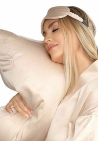 Ljusbeige sidenkudde och ögonmask. Kudden har en subtil logotyp, medan masken har ett mjukt tyg och justerbart band.