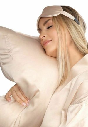 Ljusbeige sidenkudde och ögonmask. Kudden har en subtil logotyp, medan masken har ett mjukt tyg och justerbart band.