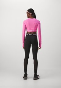 Langermet rosa treningsgenser med en cropped design. Sorte leggings har bred midjebånd med en hvit logo. Teksturert stoff gjennom hele.