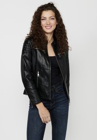 Black leather biker jacket with quilted shoulder detailing, silver zipper accents, and a fitted design. Paired with dark blue jeans.