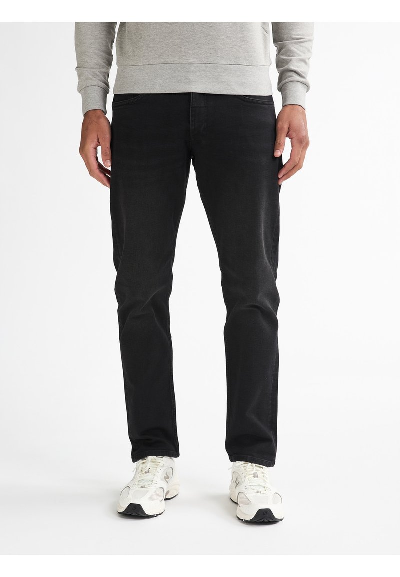 Zwarte denim jeans met een slim fit, voorzien van een medium hoge taille en een vijf-pocket ontwerp. Gecombineerd met witte sport sneakers.