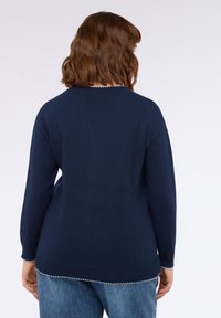 Suéter azul marino con cuello redondo y mangas largas. Presenta un dobladillo acanalado y costuras decorativas en el borde inferior. Textura suave.