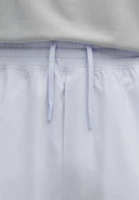 Ceinture élastique blanche avec cordons plats sur un tissu de pantalon décontracté gris clair, présenté en gros plan.