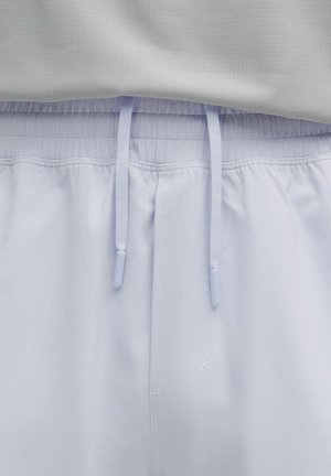 Ceinture élastique blanche avec cordons plats sur un tissu de pantalon décontracté gris clair, présenté en gros plan.