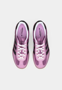 Adidas sneakers med en skinnende pink overdel, tre sorte striber, hvide snørebånd og en gummigummisål. Polstret inderside vist.