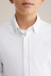 Witte geknoopte shirt gemaakt van een gestructureerde stof, met een klassieke kraag, drie knopen en een klein geborduurd logo op de borst.