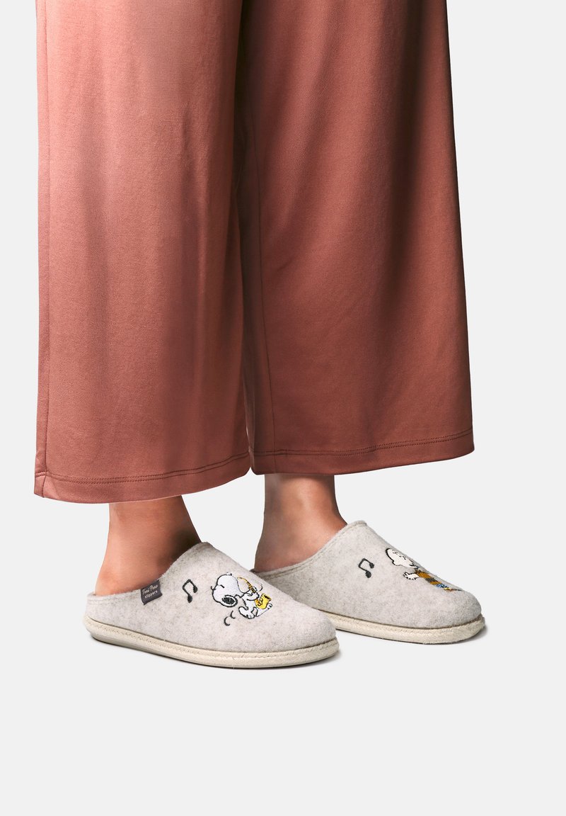 Πόδια που φορούν ανοιχτό γκρι παντόφλες slip-on με τον Snoopy και νότες μουσικής, σε συνδυασμό με χαλαρά καφέ παντελόνια.