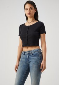 Svart kortärmad knäpptopp med texturerad fabrik och subtil GAP-logotyp. Kombineras med lätt slitna blå jeans.