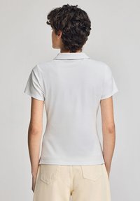 Vit polo med klassisk krage, kort ärm och figursydd design. Mjuk textur, minimalistisk detaljering, bakvy. Matchas med ljusa byxor.