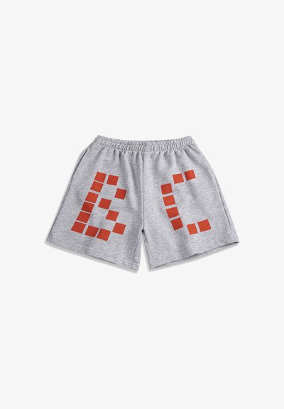 Shorts à taille élastique gris clair avec de grandes lettres rouges en style bloc, "B" sur la jambe gauche et "C" sur la jambe droite, présentés à plat.