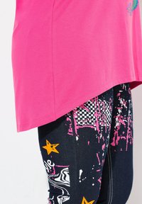 Rosa T-Shirt mit kurzen Ärmeln und abgerundetem Saum kombiniert mit schwarzen Leggings, die ein buntes, abstraktes Muster und Sterne-Details zeigen.