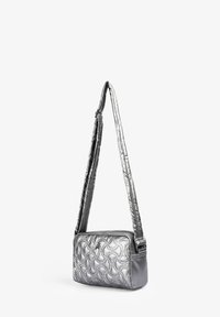 Bolso de hombro plateado acolchado con una textura suave, forma rectangular y una correa larga. Presenta detalles de costura y un cierre con cremallera.