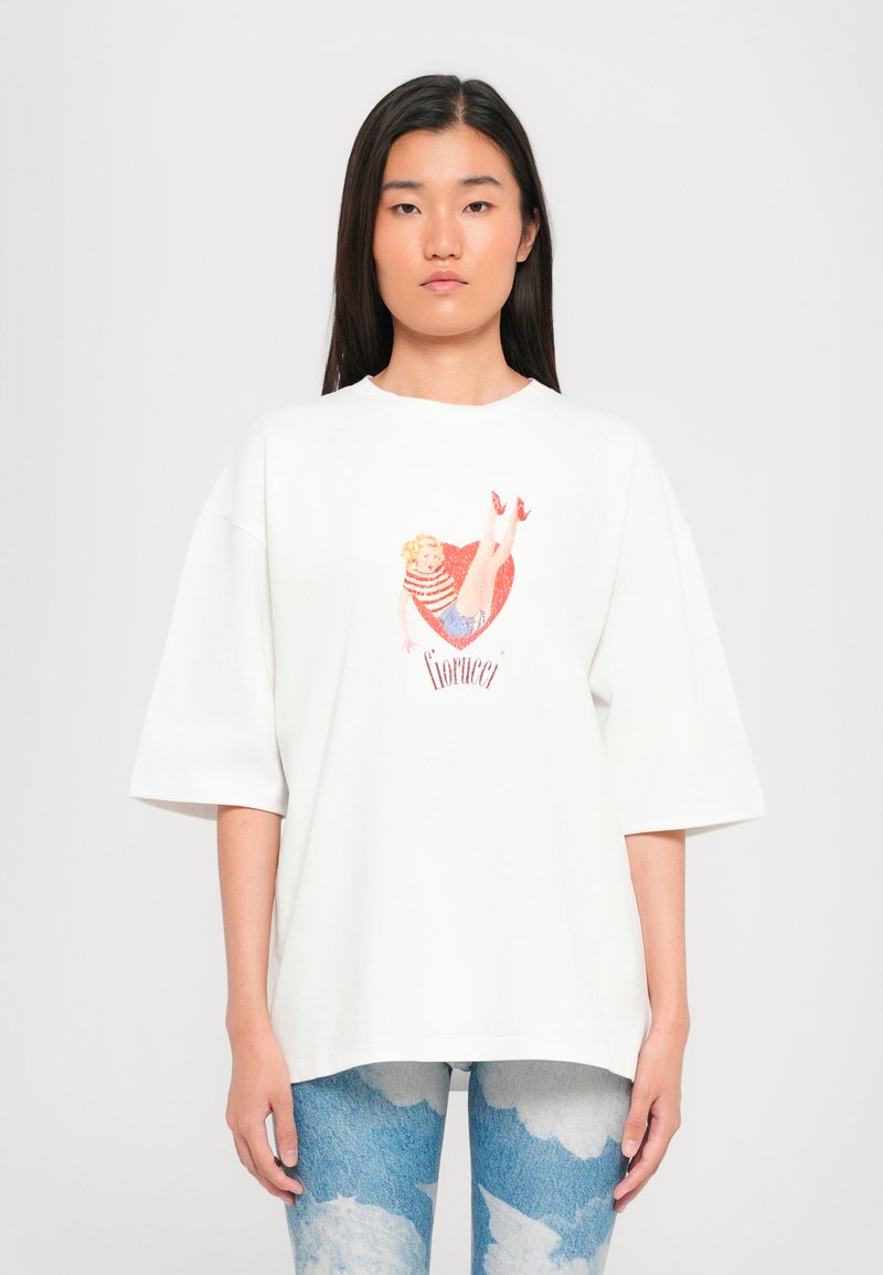 Hvit oversized t-skjorte med et fargerikt grafisk trykk av en kvinne i en stripete topp med d jeansshorts. Mykt bomullsmateriale.
