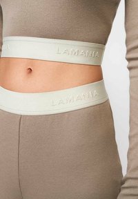 Bež ribaga crop top ja sobituvad püksid helesinise elastse vöökoha ja reljeefse tekstiga "LAMANIA."