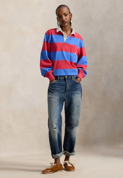 Κόκκινο και μπλε ριγέ πόλο πουκάμισο με λευκό γιακά, συνδυασμένο με ξεθωριασμένο μπλε τζιν και καφέ αθλητικά παπούτσια. Το πουκάμισο έχει τσέπη στο στήθος.