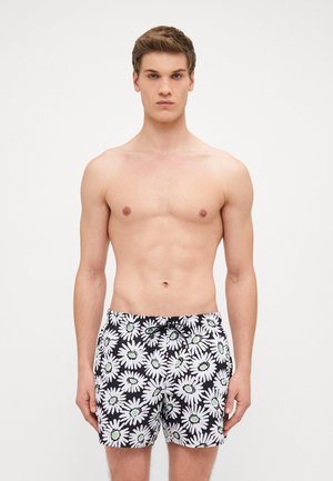 Schwarze Badehose mit weißem Gänseblümchen-Muster und grünen Mittelpunkten, aus leichtem Stoff gefertigt. Verfügt über einen verstellbaren Kordelzug am Bund.