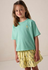 T-shirt en coton vert clair à manches courtes, avec un petit détail brodé jaune, assorti d'une jupe jaune à plusieurs couches ornée de motifs de homards.