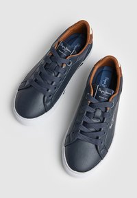 Temno modri usnjeni supergi z belimi podplati, rjavo notranjo podlogo, mornarsko modrimi vezalkami in blagovno znamko "Pepe Jeans London" na jezičku in strani.