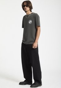 Grå bomulds t-shirt med korte ærmer og en grafik på brystet, parret med brede sorte bukser og sorte sko med teksturerede detaljer.