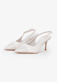 Tacones slingback de brillante cuero sintético beige. Presenta una punta afilada y una tapa mate contrastante. Tacón delgado y correa ajustable.