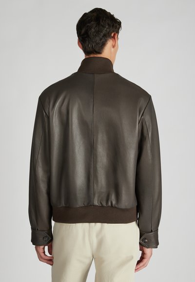 Giacca in pelle marrone con colletto e polsini a coste, design leggermente accorciato e dettagli con bottoni sulle maniche. Texture liscia.