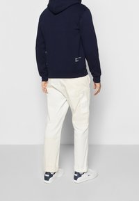 Námořnická mikina s kapucí se stahovací šňůrkou, žebrovanými manžetami a lemem. Doplněna bílými cargo kalhotami s bočními kapsami. Bílé tenisky s modrými detaily.