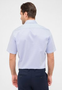 Kurzarm-Hemd in Hellblau mit kleinem geometrischem Muster, ausgestattet mit einem spitzen Kragen und glatter Stoffqualität. Kombiniert mit dunkelblauen Hosen.