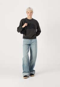 Felpa grigia scura con il testo "CRUSH", jeans a gamba larga azzurri chiari e scarpe basse nere con zeppa. Tessuto morbido, vestibilità comoda.