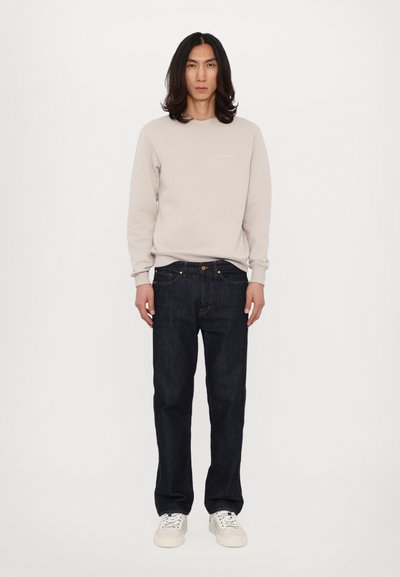 Bež sweatshirt z okroglim izrezom, v kombinaciji s temno modrimi denim hlačami in belimi supergami. Gladek material, sproščen kroj in klasična zasnova.