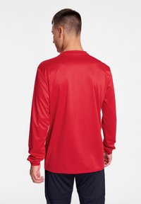 Maglietta sportiva rossa a maniche lunghe realizzata in tessuto liscio e leggero. Presenta un collo rotondo e polsini aderenti, ideale per l'abbigliamento attivo.