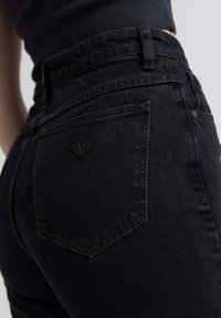 Jeans pretos de cintura alta com um tecido de denim texturizado, um patch em forma de diamante e bolsos traseiros ajustados com costura contrastante.