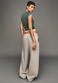 Zelený přiléhavý crop top s kontrastním výstřihem spárovaný se světlými šedými oversized tepláky s kapsami a měkkou texturou.