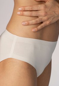 Sömlösa, höga beige trosor tillverkade av mjukt, stretchigt tyg, med en slät yta och minimalt elastiskt band i midjan.