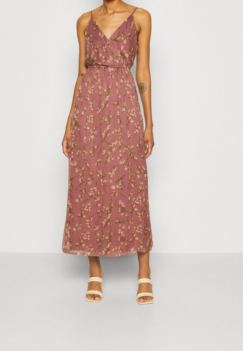Robe maxi mauve sans manches avec fines bretelles et imprimé floral, portée avec des sandales beiges à talons à bouts ouverts.
