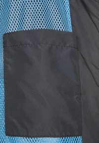 Patch rectangulaire noir cousu sur un tissu mesh bleu avec un fond en tissu noir.