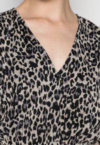 Blůza s leopardím potiskem má V-výstřih, krátké rukávy a černé knoflíky podél přední části. Látka má texturovaný, lehce splývavý charakter.