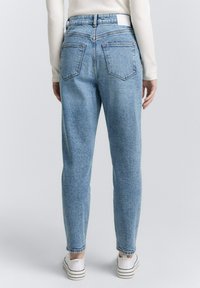 Jeans in denim azzurro chiaro a vita alta con vestibilità affusolata, dotati di due tasche posteriori e cuciture minimaliste. Tessuto morbido e design casual.