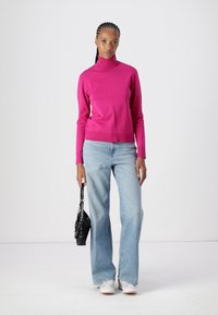 Fuchsia coltrui gecombineerd met lichtblauwe flare jeans, accessorized met een kleine zwarte tas. Glad stoffen, casual pasvorm.