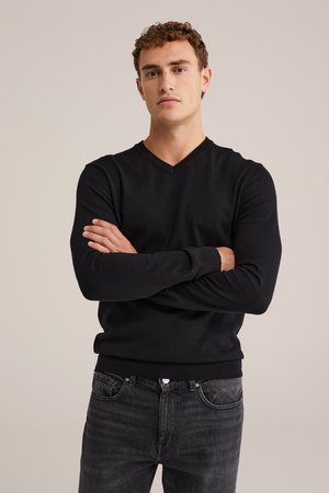 Zwarte v-hals trui van lichtgewicht stof, met lange mouwen en een getailleerd ontwerp, gecombineerd met donkergrijze jeans.
