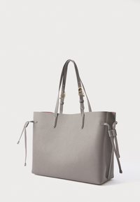 Šedá texturovaná kožená taška na rameno se dvěma horními uchy, nastavitelnými postranními šňůrami a kontrastním červeným vnitřkem. Má zlaté kovové doplňky.