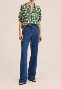 Grøn og cremefarvet mønstret bluse med krave, kombineret med højtaljede blå viddejeans og sorte sandaler. Glat tekstur, afslappet pasform.