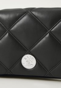 Svart kviltad syntetläderväska med diamantmönster och en rund silverlogotyp. Slät textur med kontrasterande sömdekorationer.